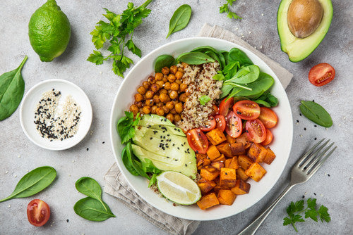 Healthy salad bowl with quinoa, chickpeas, avocado, and vegetables on a gray surface.