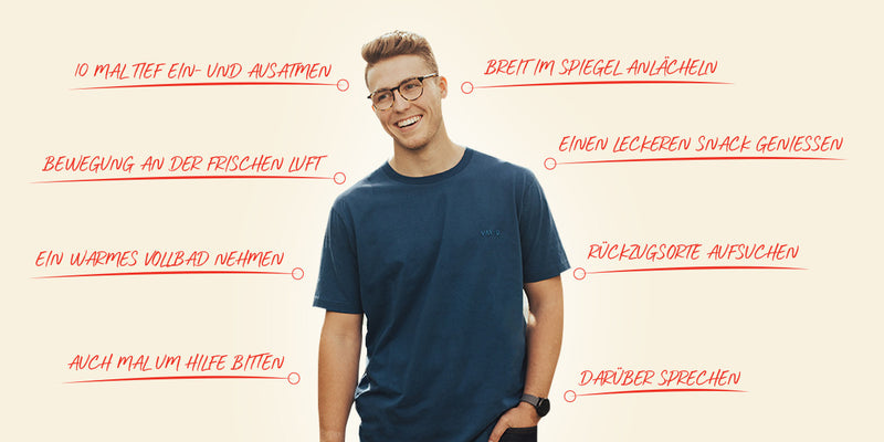 Man wearing glasses and a blue shirt standing against a light background with text in German.