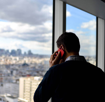 Person talking on a red phone in front of a large window with a cityscape view