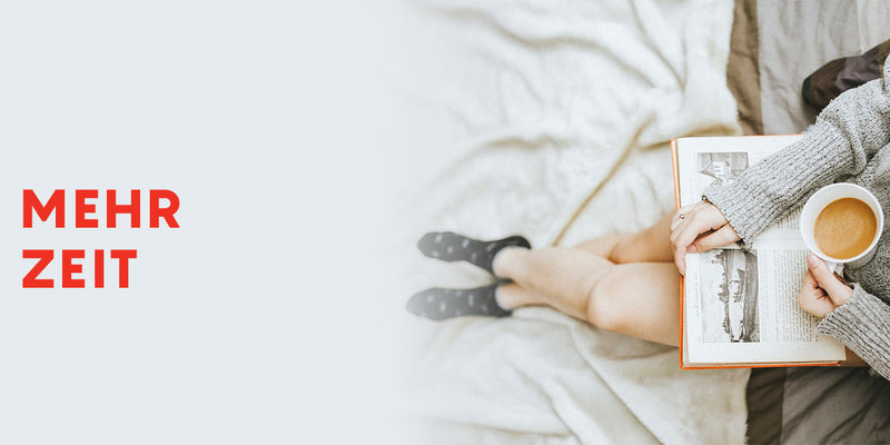 Person sitting on a bed holding a book and a cup with 'Mehr Zeit' text on a light background