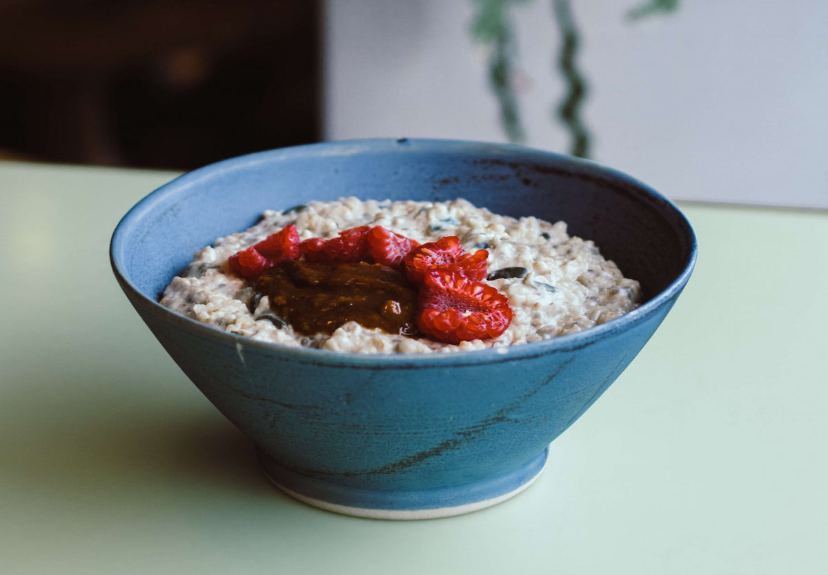 Blue ceramic bowl with oatmeal and red toppings on a light green surface.