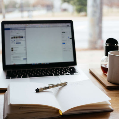 Laptop with open notebook and pen on a desk